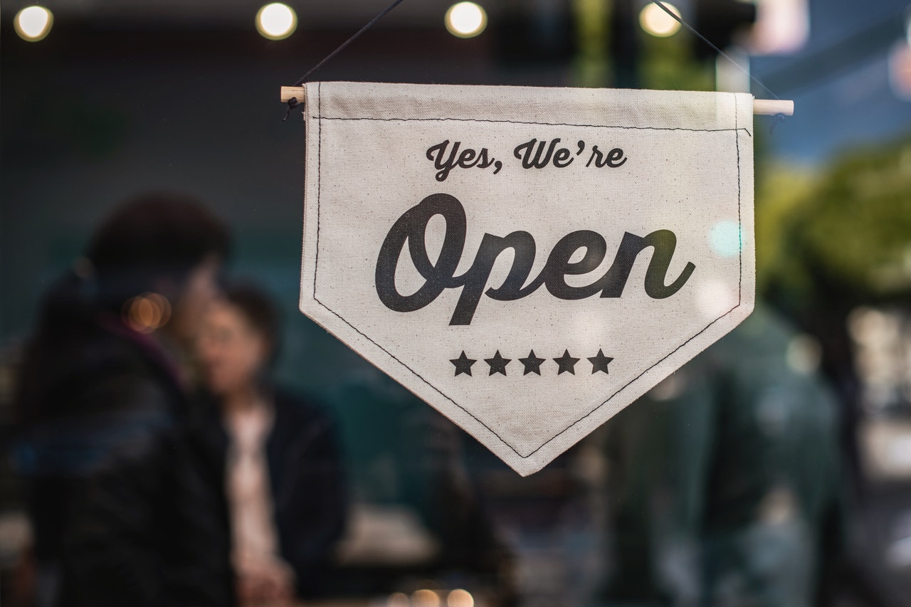 Open sign displayed in a restaurant window, indicating business readiness, with blurred figures of customers